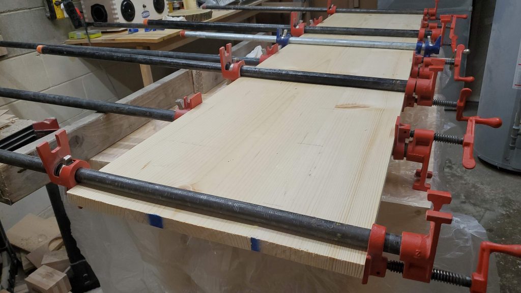 Photo of two pine planks grues together using bar clamps
